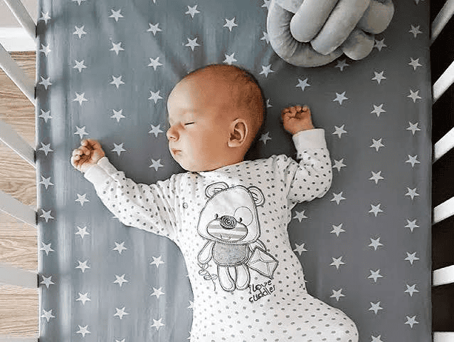 Bebê dormindo de barriga para cima no berço, com estrelas ao redor, ilustrando o sono seguro