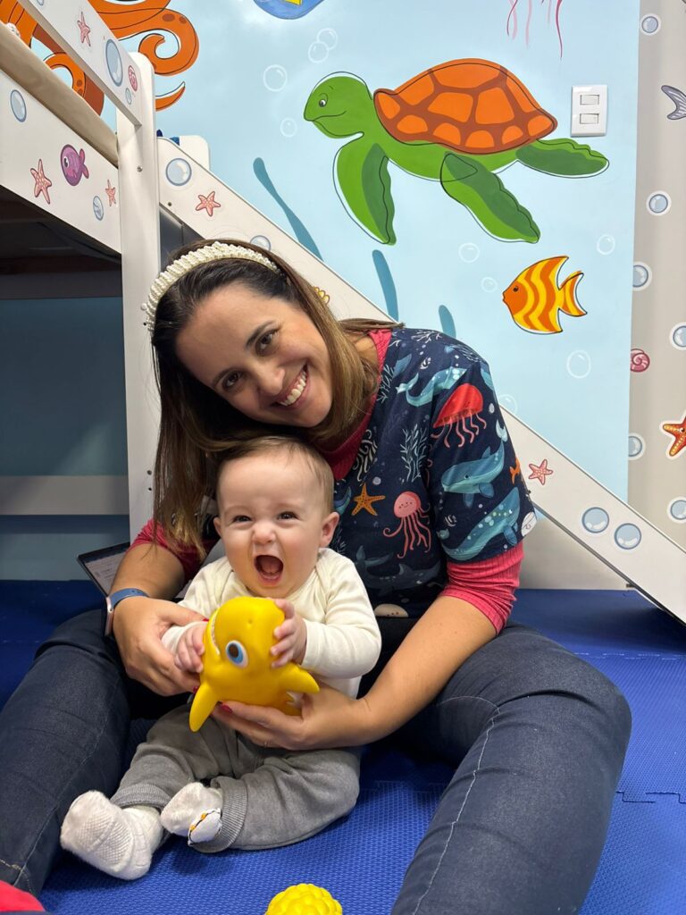 Dra. Patty Terrível com bebê sorrindo segurando brinquedo